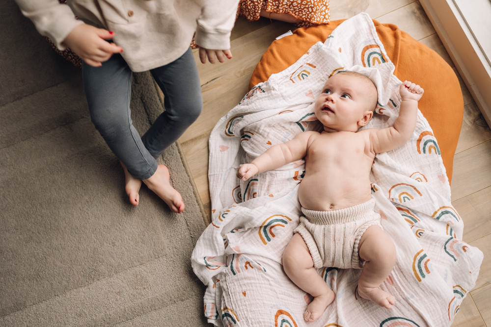 Baby on a rainbow coloured swaddle looking up at his little sister.