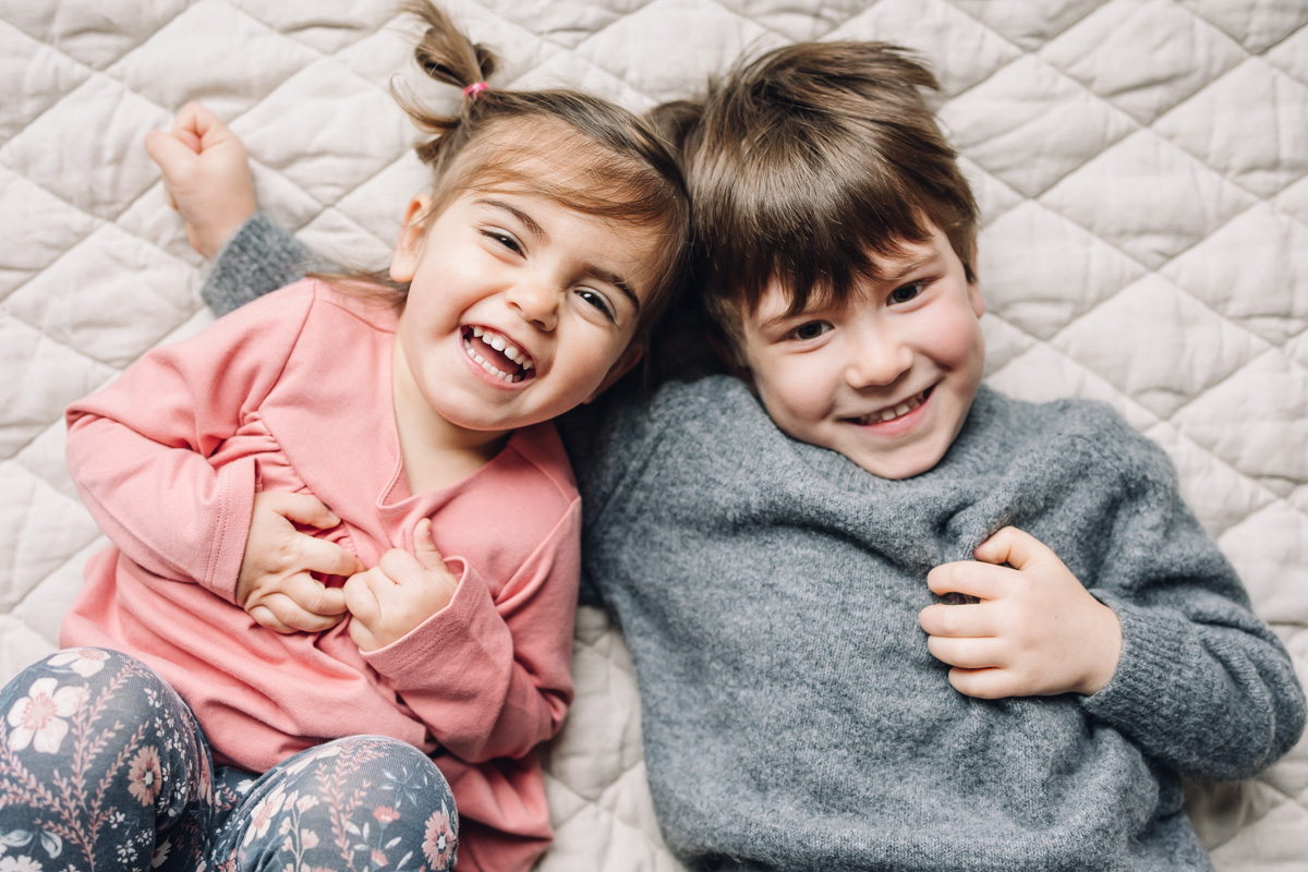 A little girl and boy are lying on their back and looking at the camera smiling by a Montreal Photographer.