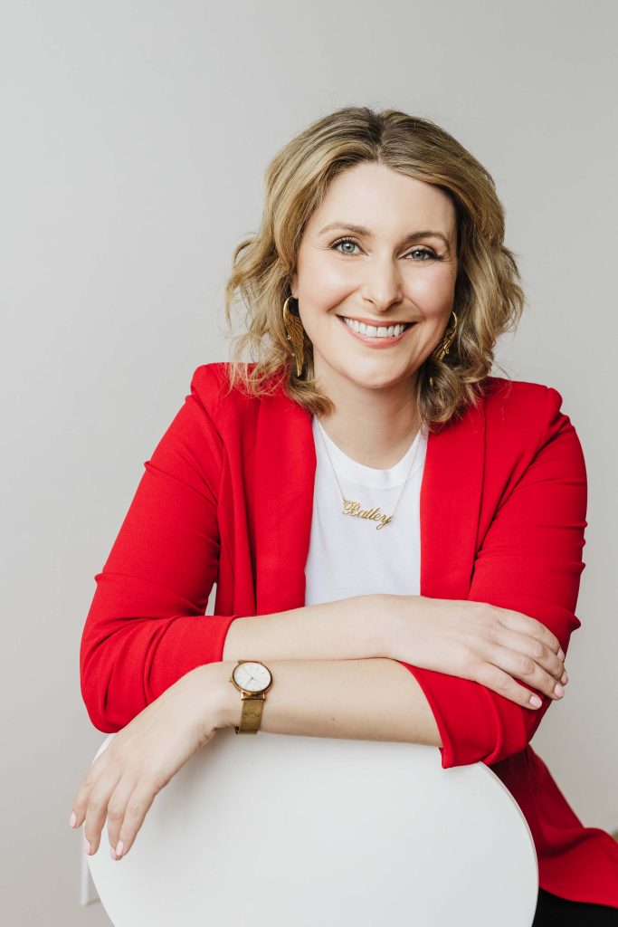 Lady in bright red blazer and shoulder length blonde hair smiling and looking at the camera.